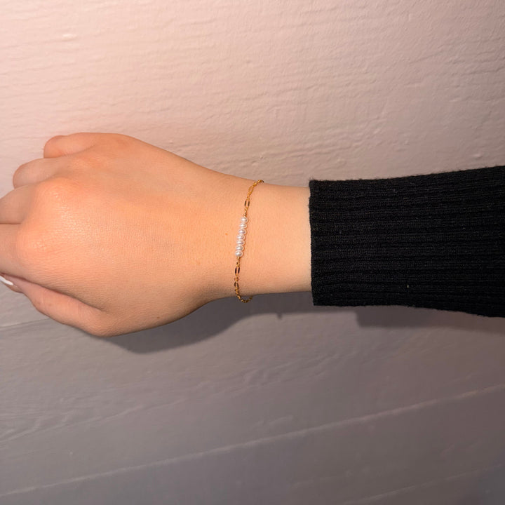 Hand wearing a gold bracelet on a plain background