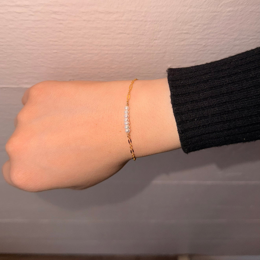 Hand wearing a gold bracelet on a plain background
