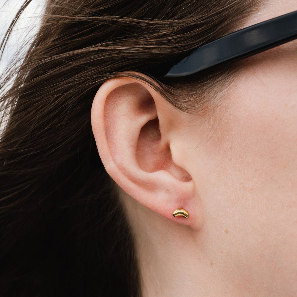 Close-up of an ear with a gold earring and sunglasses on the head.