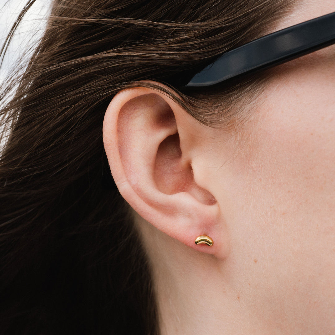 Close-up of an ear with a gold earring and sunglasses on the head.