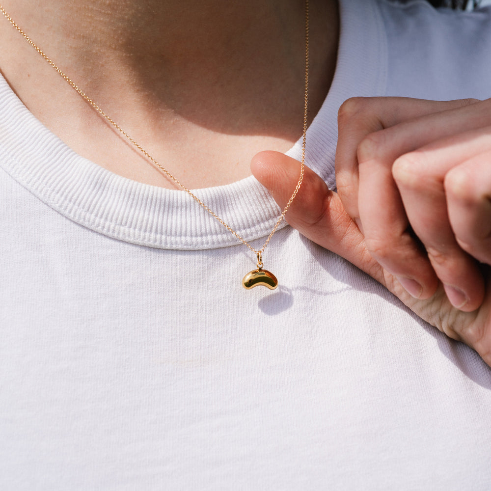 Person wearing a gold necklace with a small pendant on a white shirt