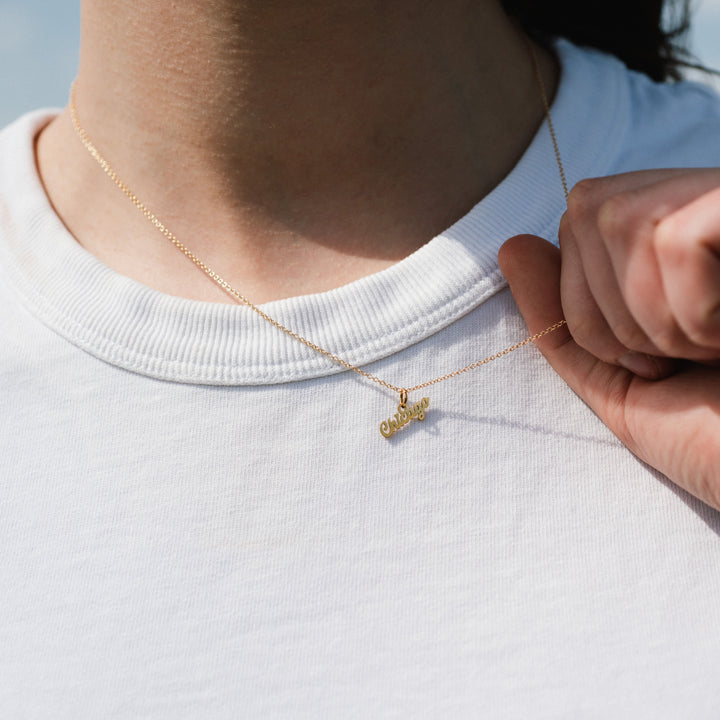 Person wearing a gold necklace with a pendant on a white shirt