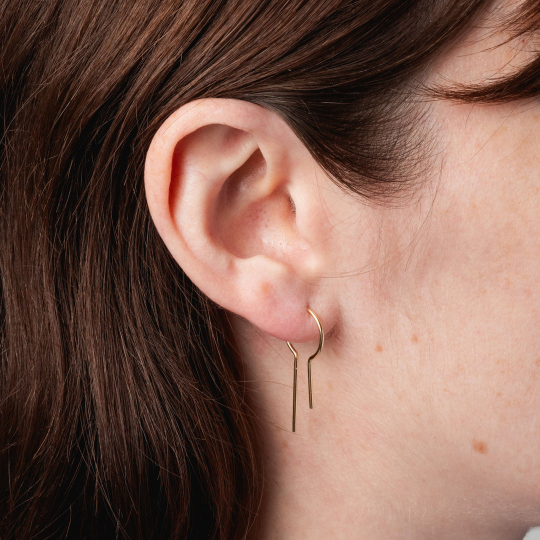 Close-up of an ear wearing a gold hoop earring with hair partially covering the frame.