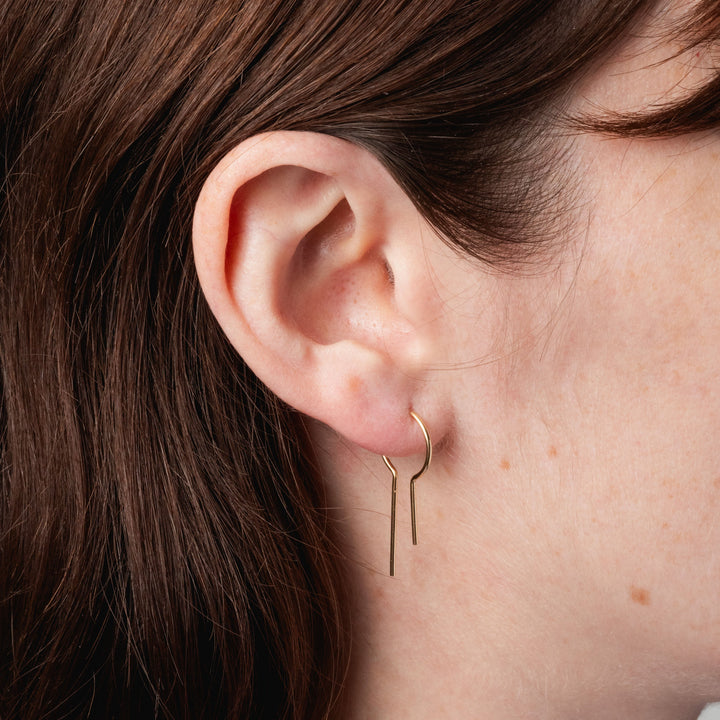 Close-up of an ear wearing a gold hoop earring with hair partially covering the frame.