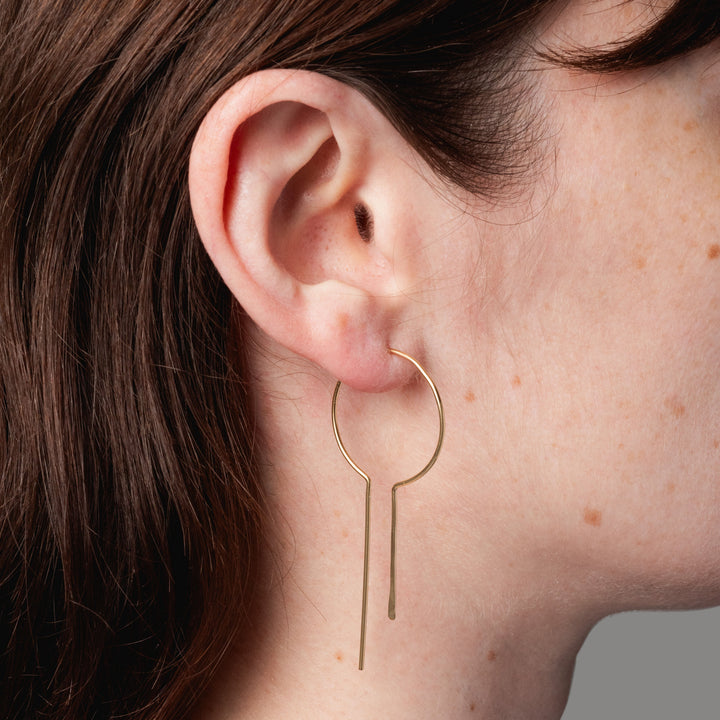 Close-up of a person wearing a gold hoop earring with a gray background