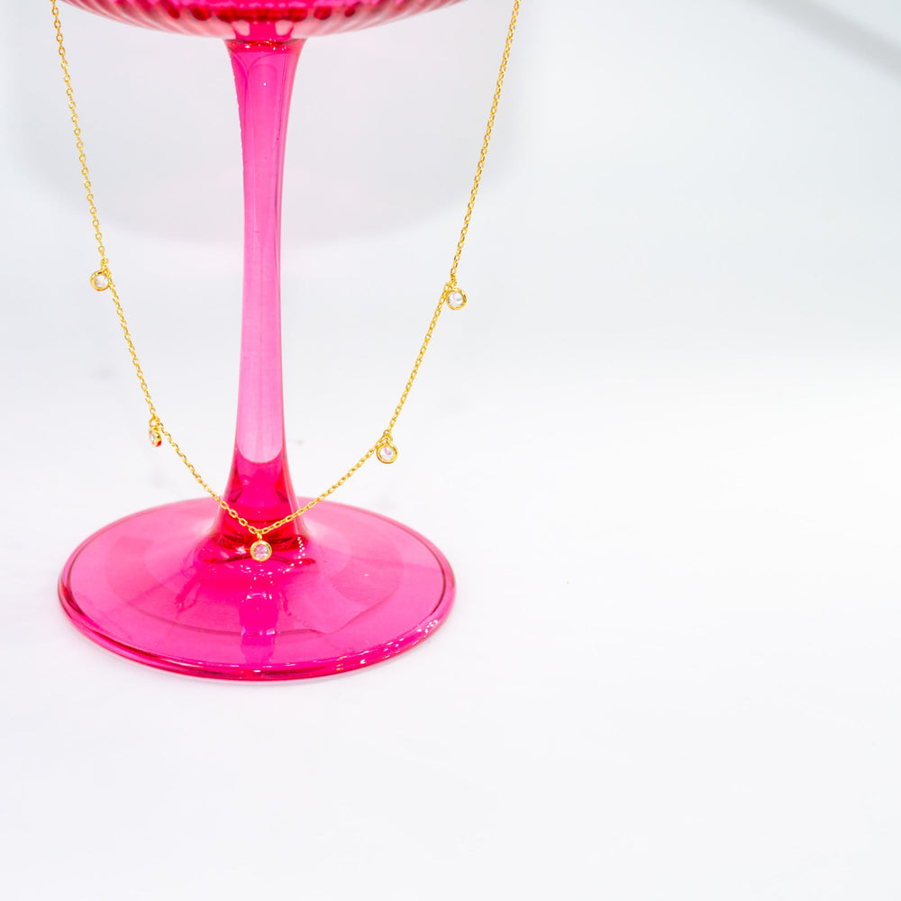 Pink glass object with a gold necklace draped over it on a white background