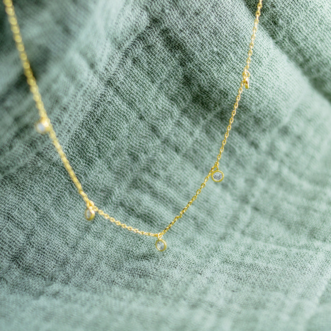 Gold necklace with small pendants on a textured green fabric background