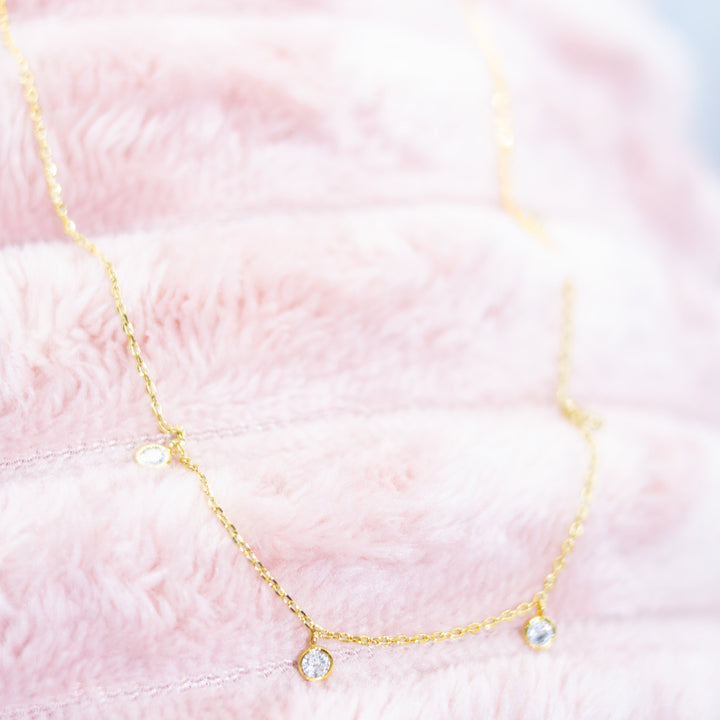 Gold necklace with small round pendants on a pink textured background