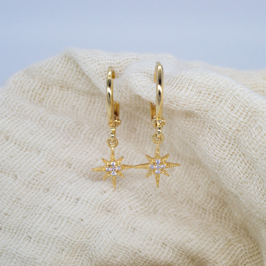 Gold hoop earrings with star-shaped charms on a textured beige surface