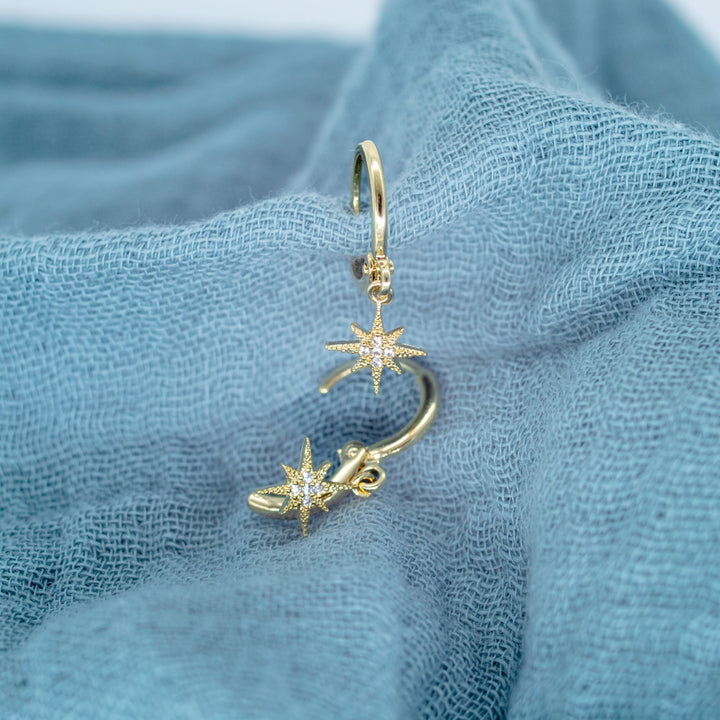 Gold hoop earrings with starfish charms on a blue fabric background