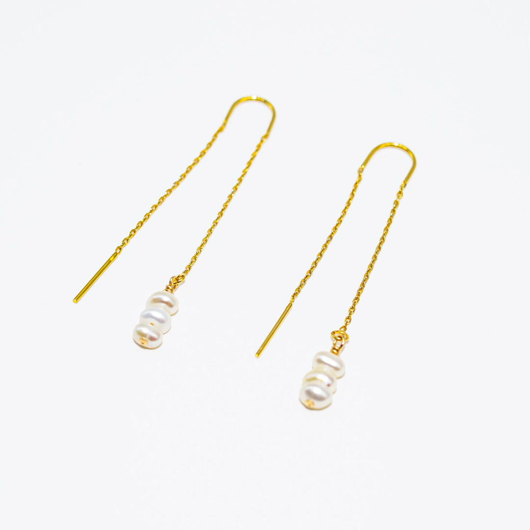 Pair of gold threader earrings with pearl-like beads on a white background