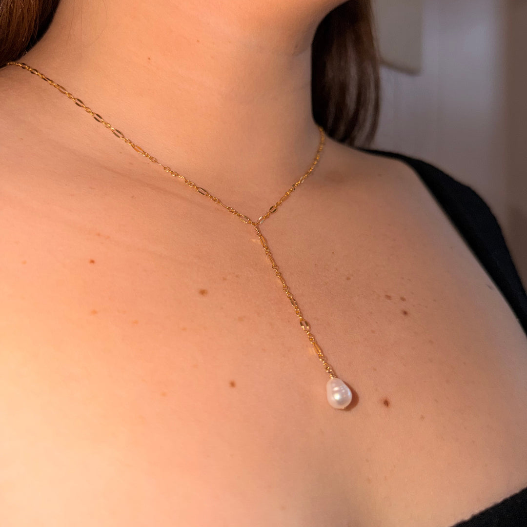 Gold necklace with a pearl pendant worn by a person