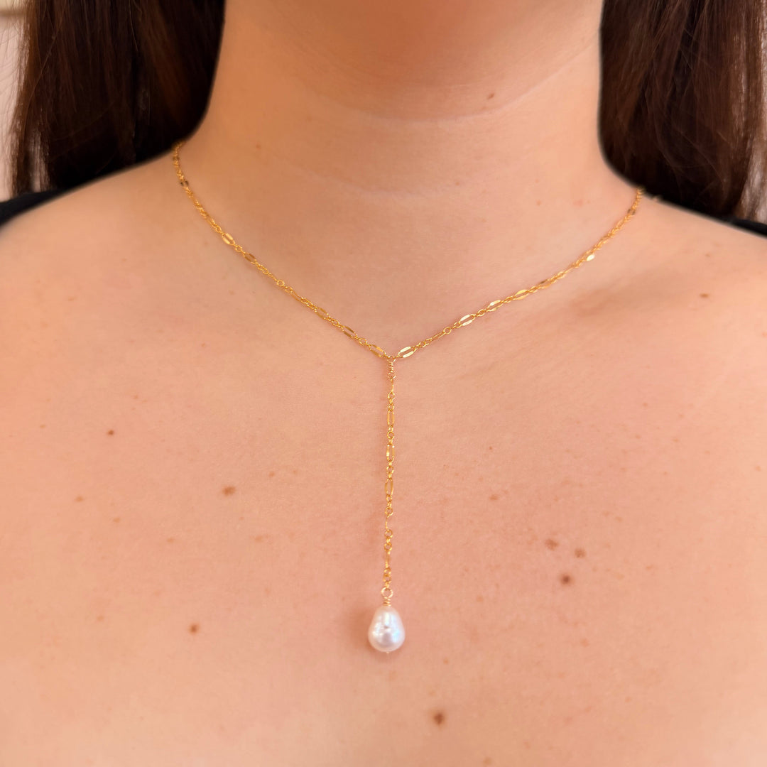 Gold necklace with a pearl pendant worn by a person