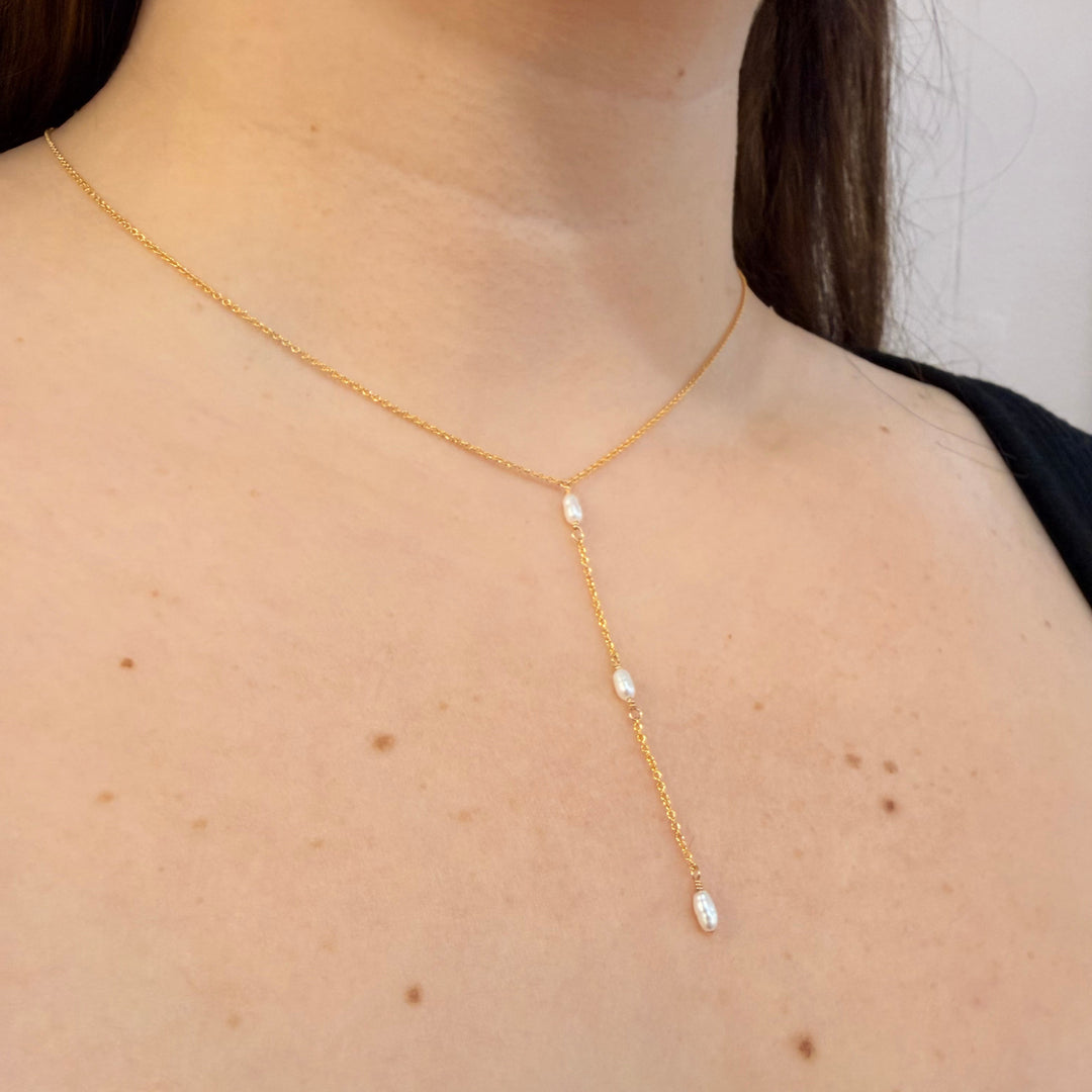 Gold necklace with small pearls on a person's neck against a neutral background