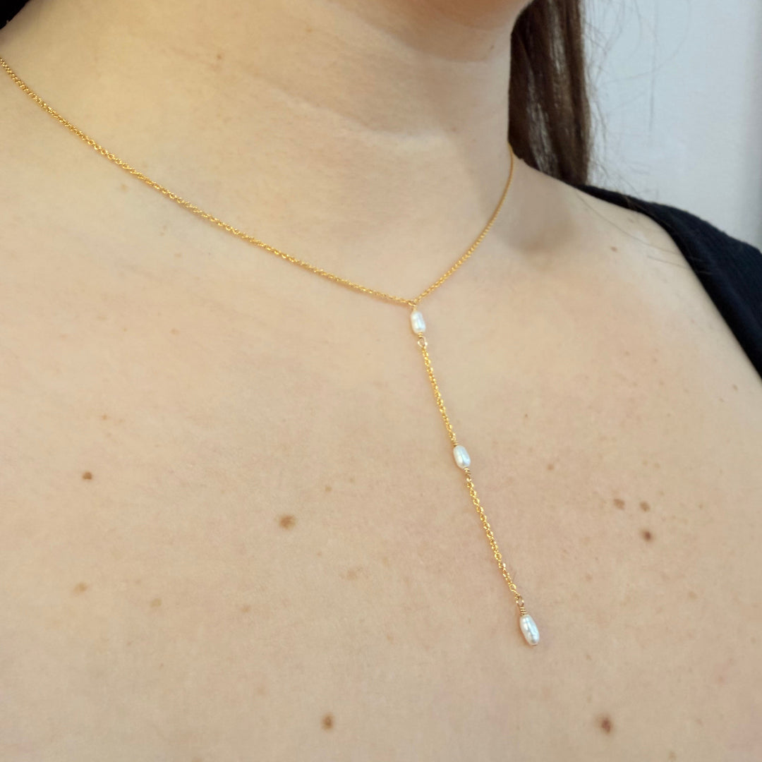 Gold necklace with pearls on a person's neck against a neutral background