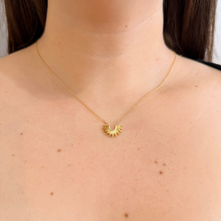 Gold necklace with a sun pendant worn by a person