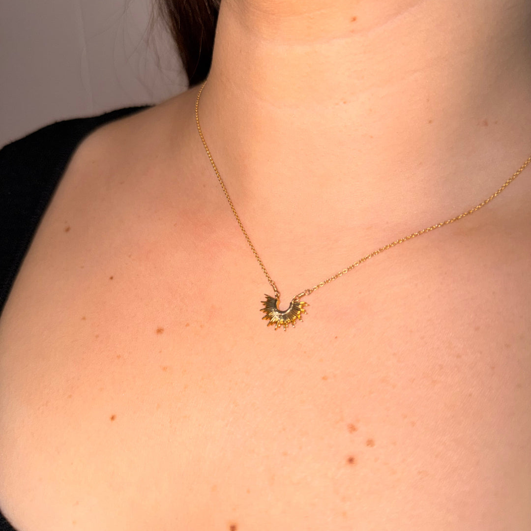 Necklace with a sun pendant worn by a person against a neutral background