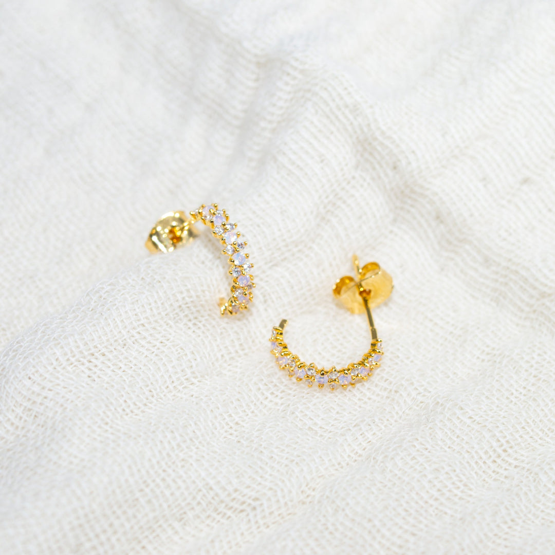 Gold hoop earrings with small diamonds on a white textured background