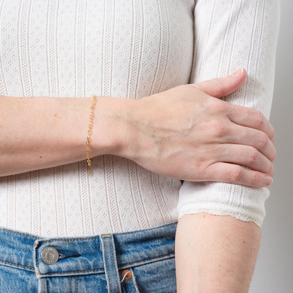 Person wearing a gold bracelet on a plain background