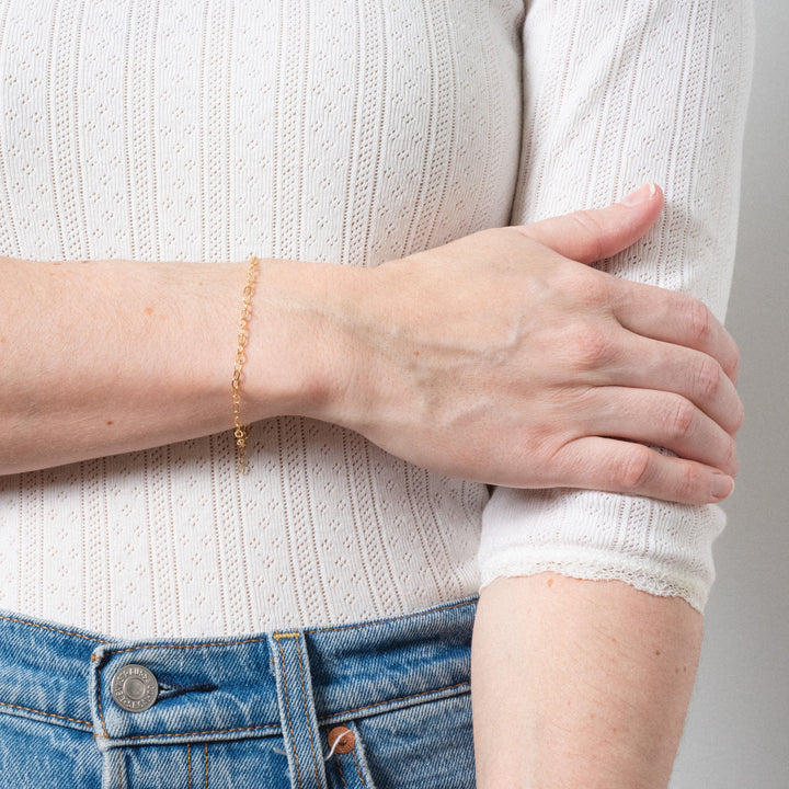Person wearing a gold bracelet on a plain background