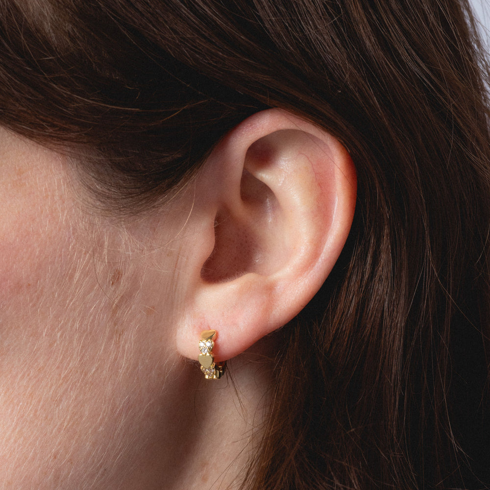 Close-up of an ear wearing a gold hoop earring with hair partially covering the frame.