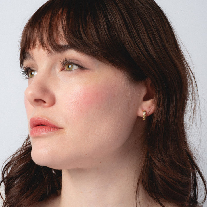 Woman wearing a gold earring against a plain background
