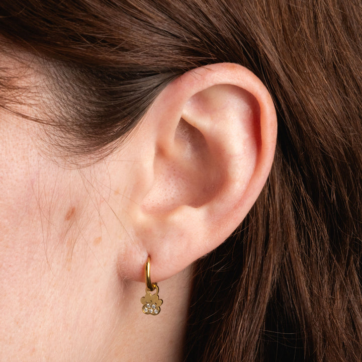 Close-up of an ear wearing a gold earring with a paw print design.