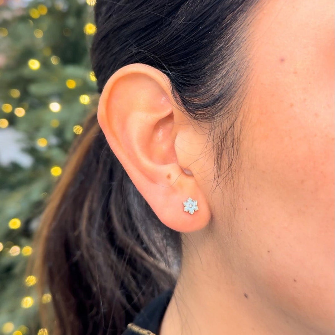 Close-up of an ear wearing a star-shaped earring with a blurred Christmas tree background